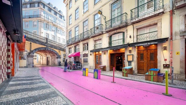 Een straat met een roze fietspad, een café en een gebouw met een bord waarop 