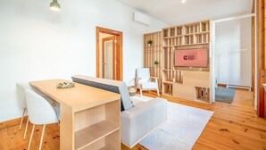 Een moderne kamer met een houten eettafel, witte stoelen, een bank, een televisie en een houten boekenkast.