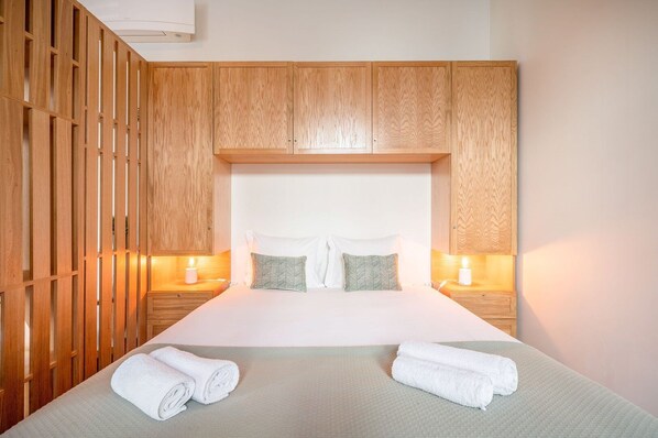 A hotel room with a large bed, wooden headboard, two bedside tables with lamps, and a wooden partition.