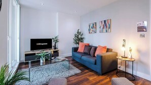 Un salon moderne comprenant un canapé, une table basse, un téléviseur et une petite table d’appoint avec une lampe.