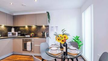 A modern kitchen with a dining area, featuring a glass table, chairs, and a vase with flowers.