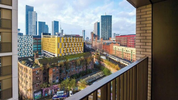 Une vue urbaine avec des bâtiments modernes, un immeuble jaune portant l’inscription « Energy Brothers », et un train au premier plan.