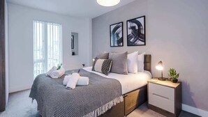 Une chambre à coucher moderne avec un lit, une table de chevet, une lampe et une œuvre d’art.