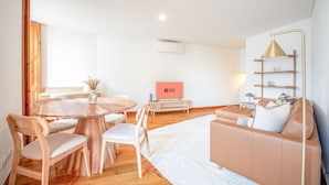 A modern living room with a round wooden table, two chairs, a sofa, and a TV. - GuestReady - Night out adventure in Lisbon (Lisbon)