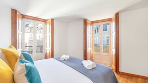 A hotel room with a large bed, two windows with wooden frames, and a view of buildings outside. - GuestReady - Night out adventure in Lisbon (Lisbon)