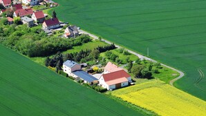 An aerial view of a rural area with houses and fields, including a large field of yellow flowers.