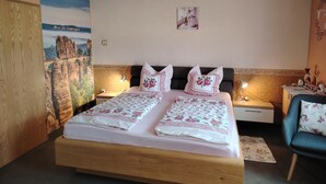 A double bed with floral bedding, two bedside tables with lamps, a nightstand, a chair, and a mural of a bridge on the wall.