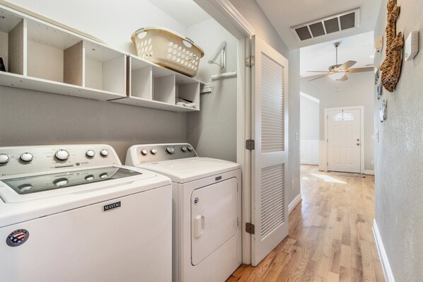 Een wasruimte met twee Maytag wasmachines en drogers, een plafondventilator en een mand op een plank.