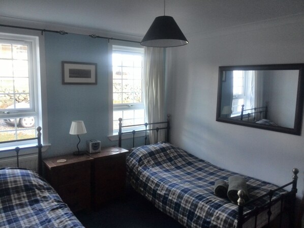 Un dormitorio con dos camas, una mesita de noche con lámpara, un espejo y una ventana con cortinas.