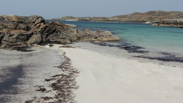 A rocky beach with clear turquoise water and white sand.