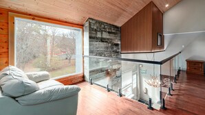 Un interior moderno con techo de madera, barandilla de vidrio, un sofá y una decoración con cabeza de venado.