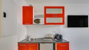 Una cocina compacta con armarios rojos, un microondas, un hervidor y una tostadora.