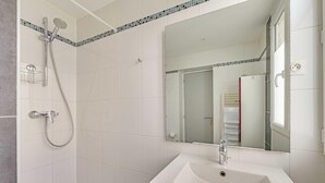 Un baño con lavamanos blanco, espejo, ducha con cabezal de ducha manual y pared con azulejos.