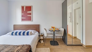 Una habitación de hotel con cama, una pequeña mesa de comedor con sillas, un espejo y un armario.