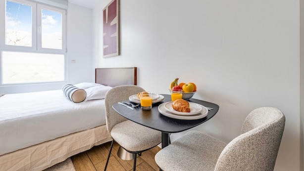 Una habitación de hotel con una cama, una mesa de desayuno con platos, vasos y un bol de fruta.