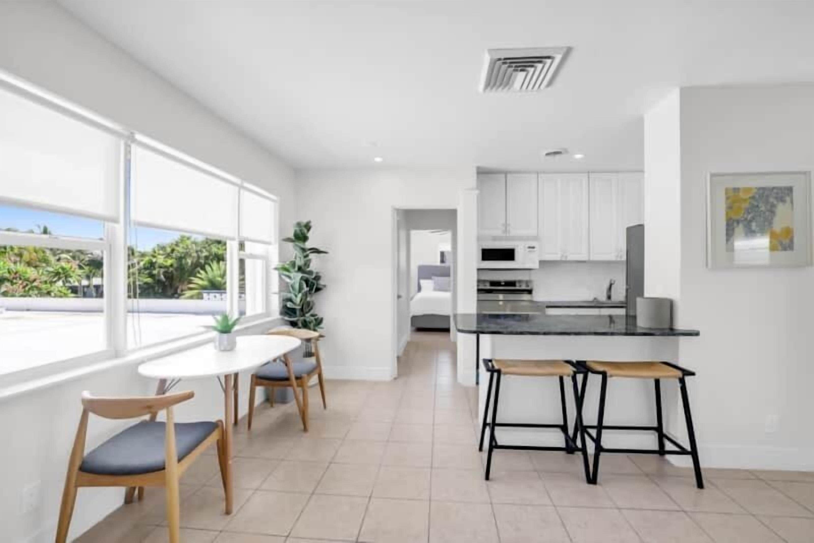 A modern kitchen with white cabinets, a black countertop, and a dining area with a round table and chairs.