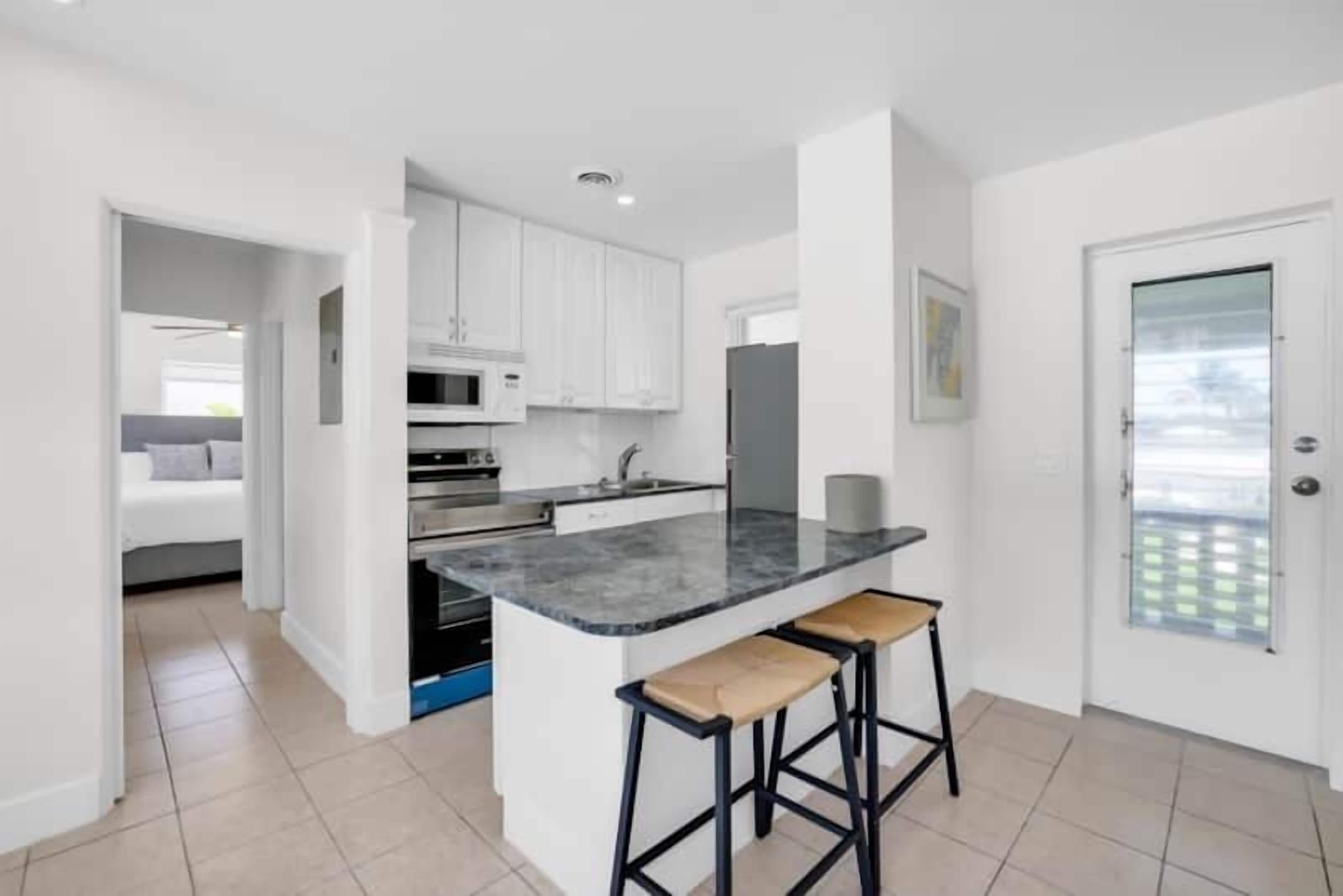 A modern kitchen with white cabinets, a black countertop, and two bar stools.