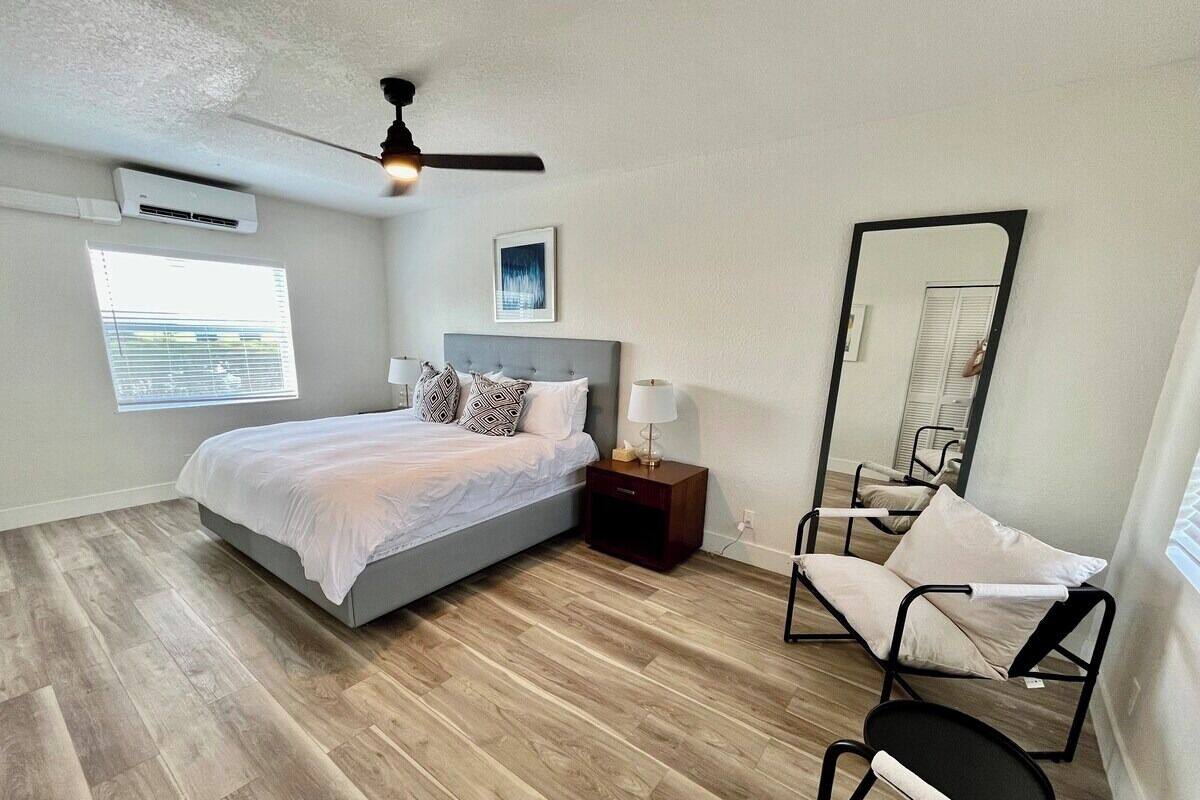 Un dormitorio con cama, mesita de noche, silla, espejo y ventilador de techo.