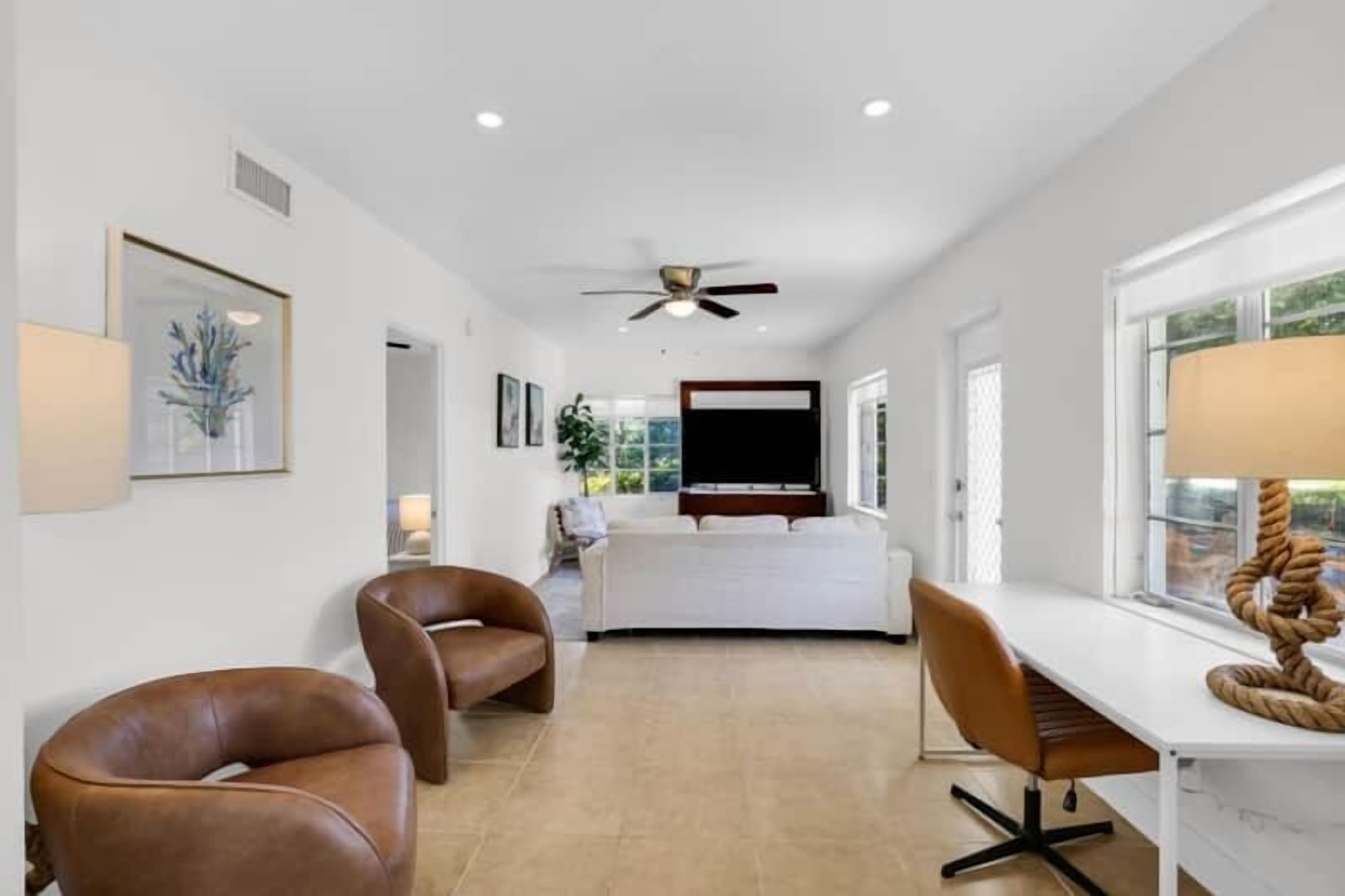 A modern interior with a white sofa, brown leather chairs, a dining table, and a ceiling fan.