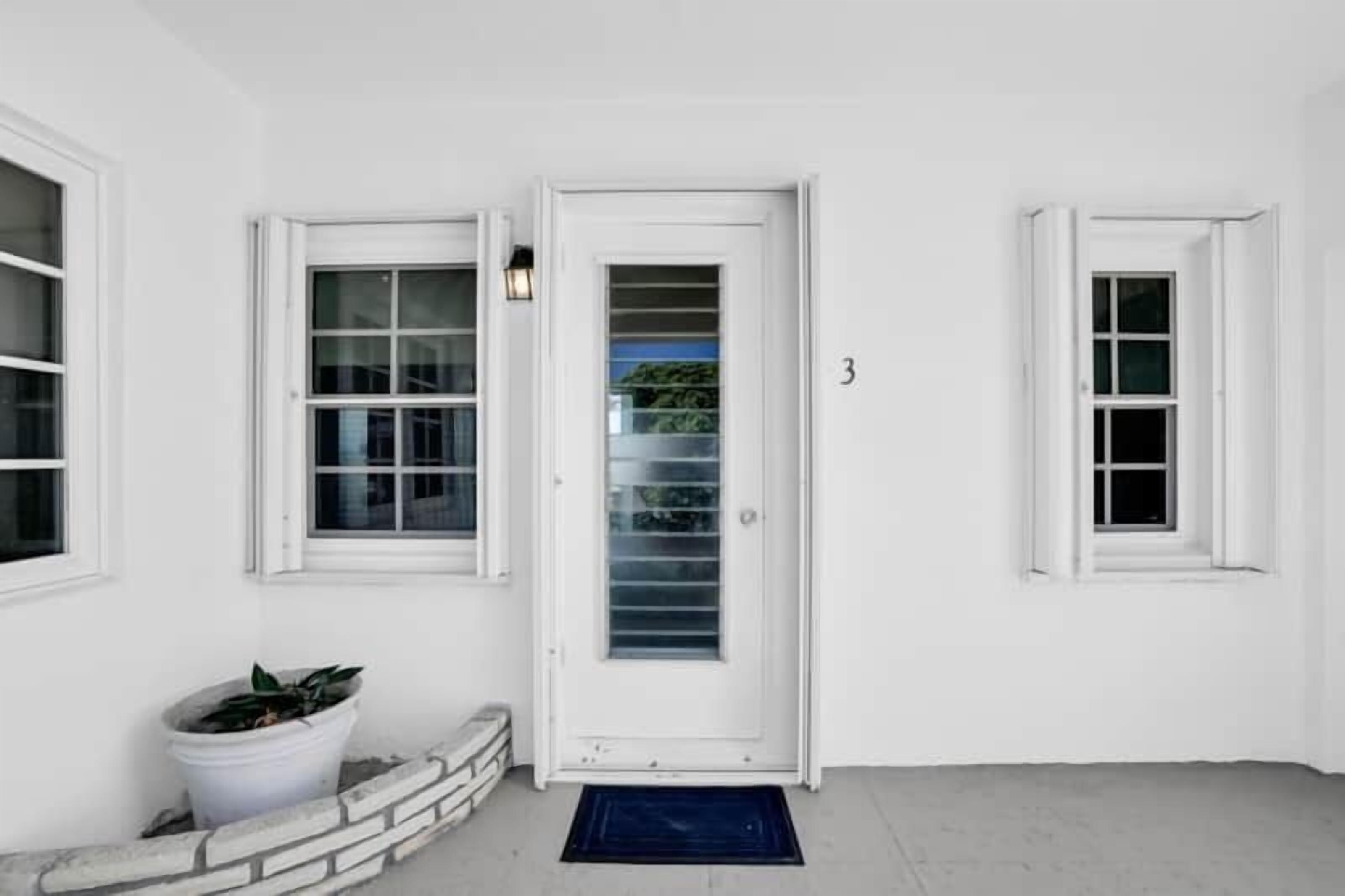 A white exterior with a door, two windows, and a potted plant.