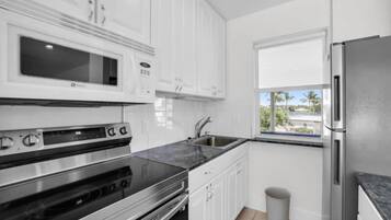 A modern kitchen with white cabinets, a stainless steel refrigerator, a built-in microwave, and a window with a view of palm trees.