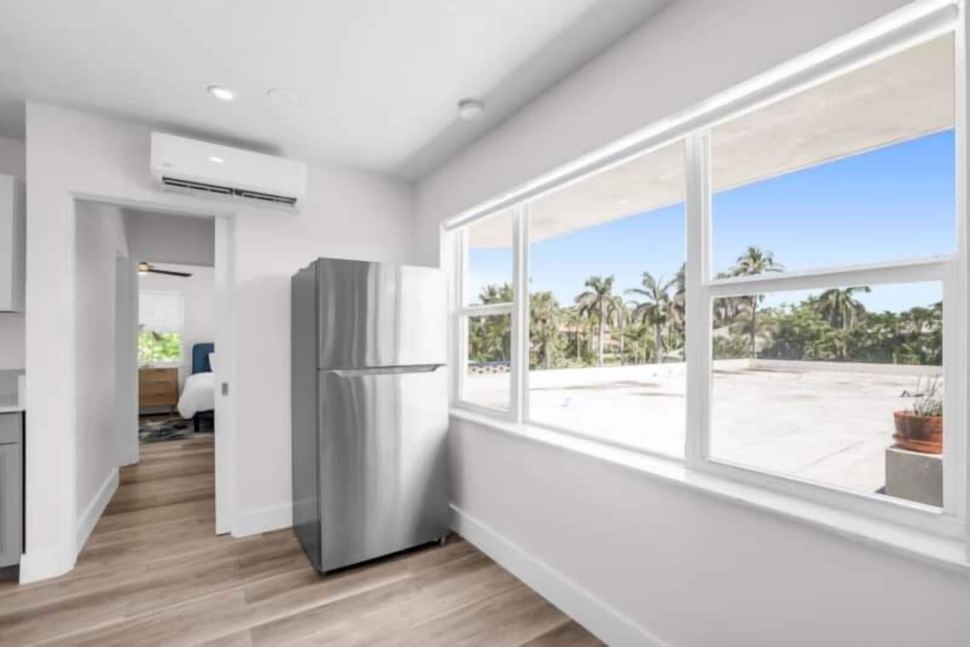 A modern kitchen with a large window, a built-in refrigerator, and a view of a tropical outdoor area.
