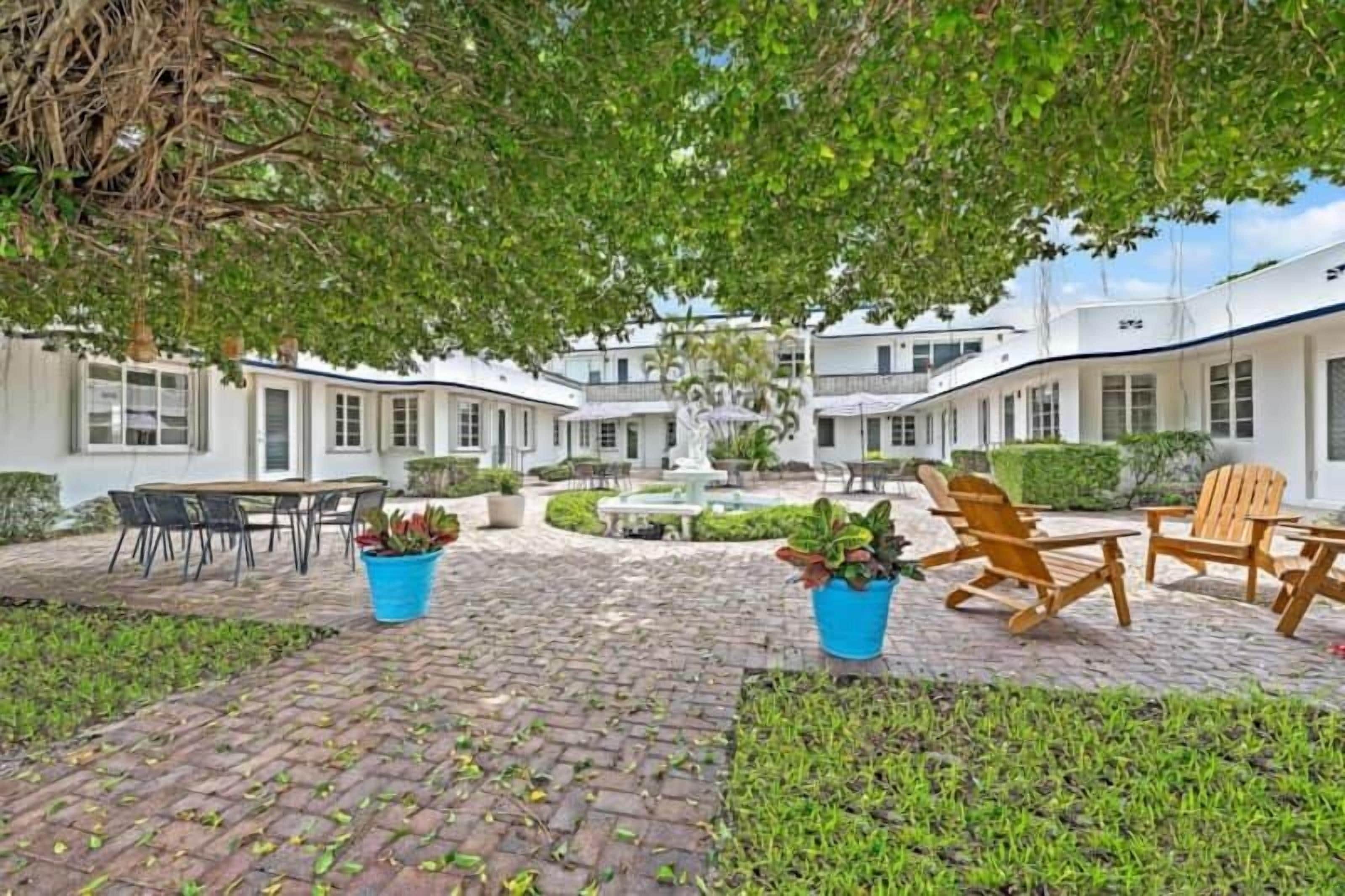 A courtyard with outdoor seating, a fountain, and a white building with multiple windows.