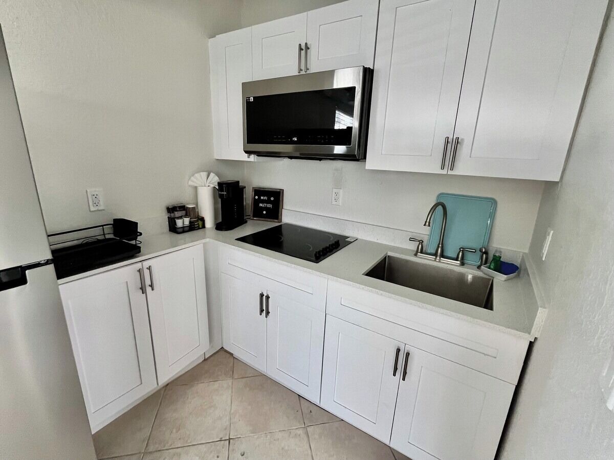 A compact kitchen with white cabinets, a stainless steel microwave, a coffee maker, and a sink.
