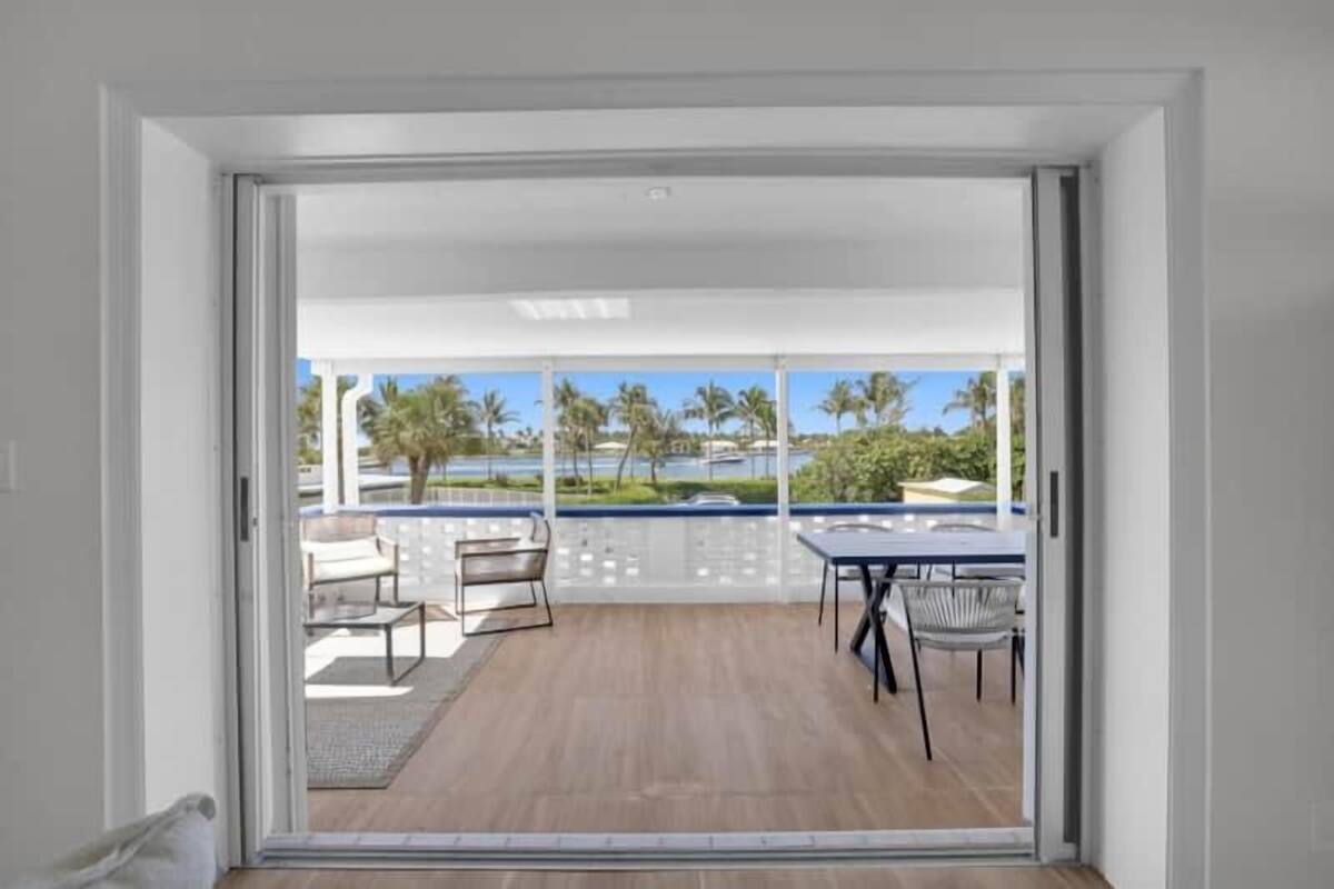 Un balcón moderno con piso de madera, barandal blanco y una mesa con sillas.