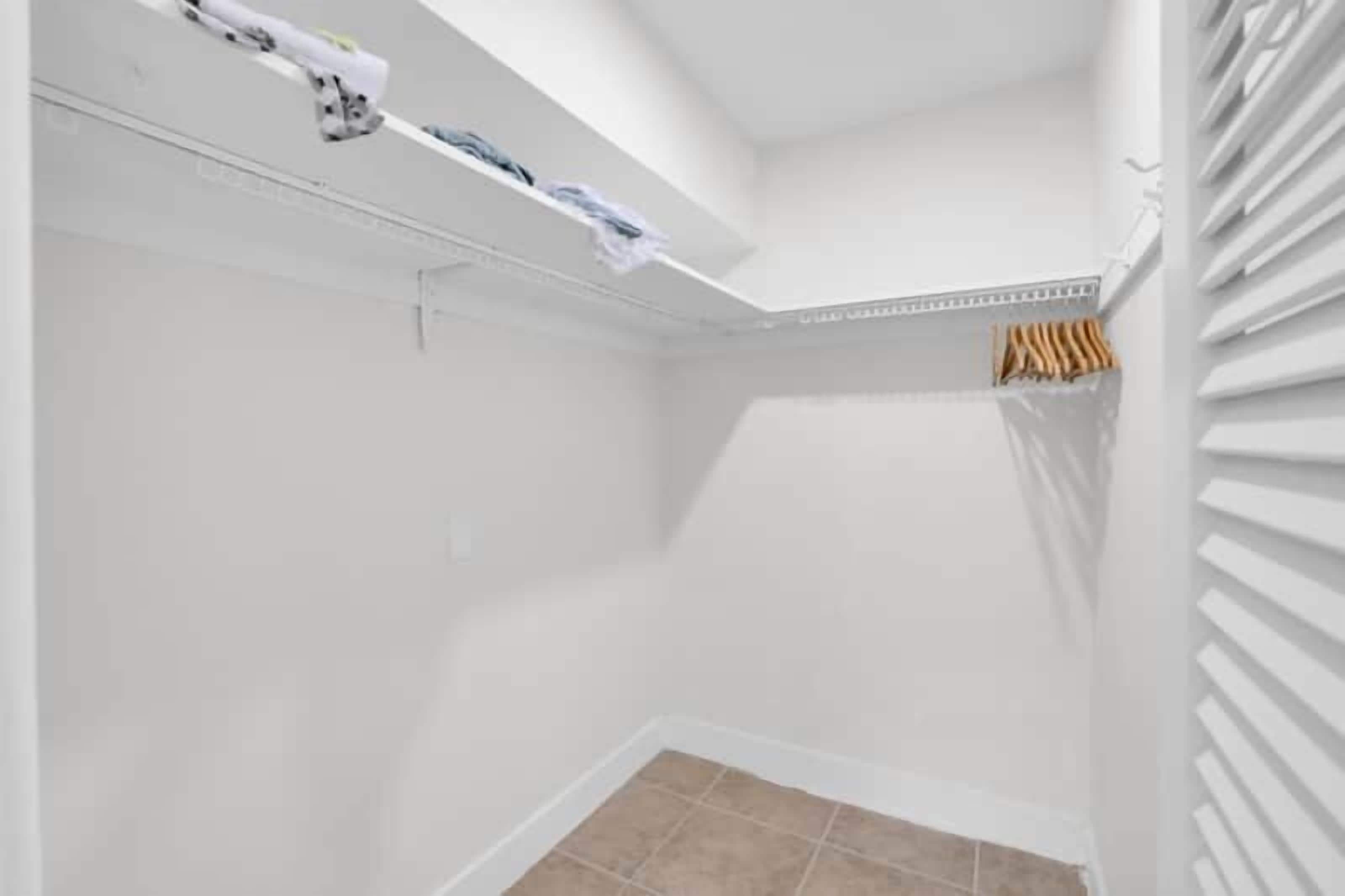 Una habitación con paredes blancas, piso de baldosas, ventilador de techo y un perchero.
