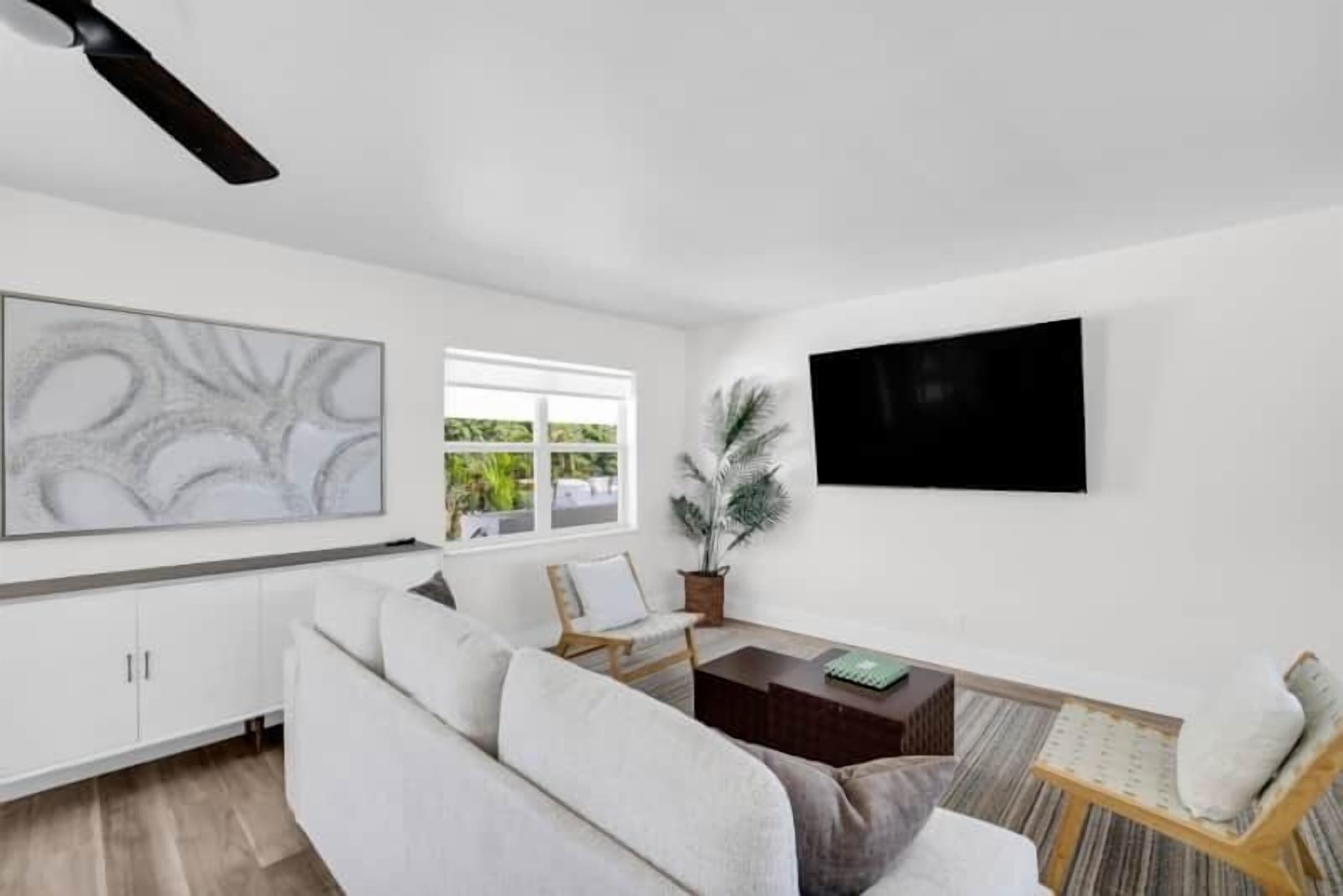 Uma sala de estar moderna com um sofá branco, uma mesa de centro de madeira e uma televisão de tela plana fixada na parede.