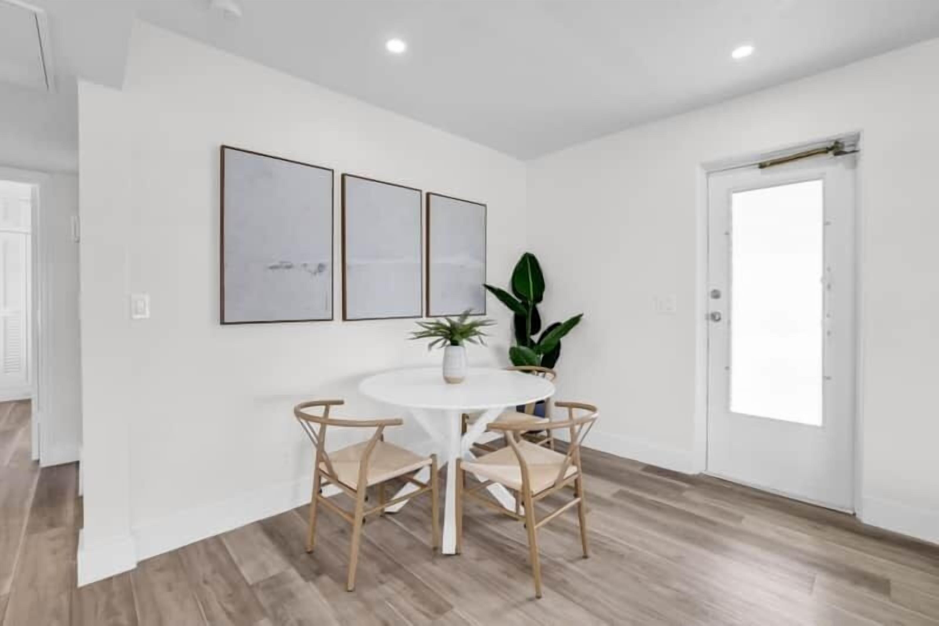 A dining area with a round table, four chairs, and three framed pictures on the wall.