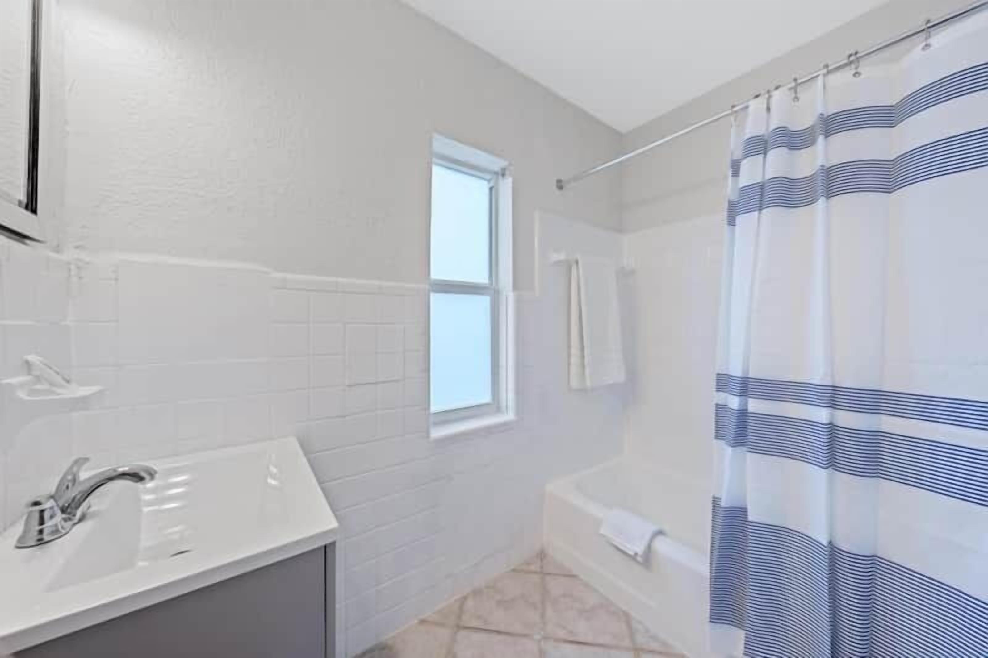 A bathroom with a white sink, a window, and a shower curtain.