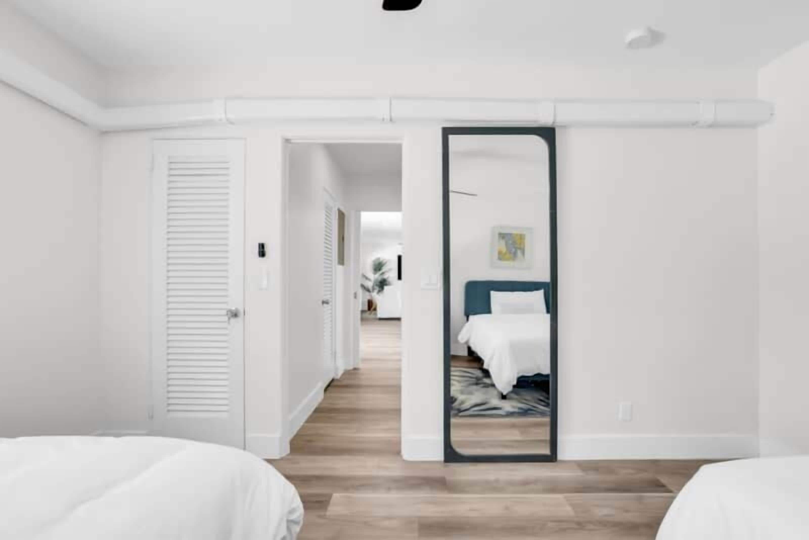 Habitació d'hotel moderna amb un mirall gran, un llit amb roba de llit blanca i un paviment de fusta.