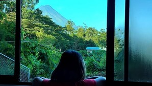 A person sitting by a window with a view of a mountain and lush greenery. - Villa Perezosa (sloth) (La Fortuna)