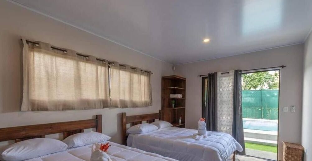 A hotel room with two beds, a wooden headboard, a small shelf, and a sliding glass door leading to a balcony. - Villa Perezosa (sloth) (La Fortuna)