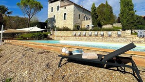 Un bâtiment en pierre doté d’une piscine, de chaises longues et d’une pergola.