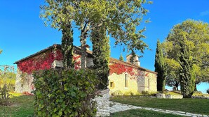Un bâtiment en pierre avec un mur recouvert de vigne rouge, un chemin en pierre et un ciel bleu clair.