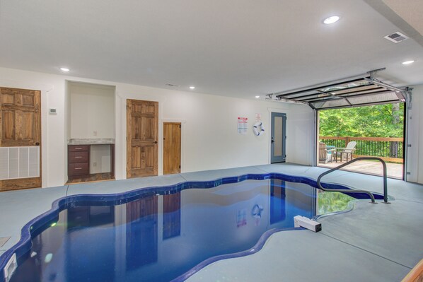 A swimming pool with a clear blue water feature, wooden cabinets, and a view of a patio with outdoor furniture. - Aqua Vitae (Gatlinburg)