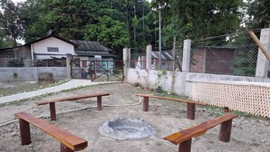 A fenced outdoor area with four wooden benches arranged in a circle around a central fire pit.