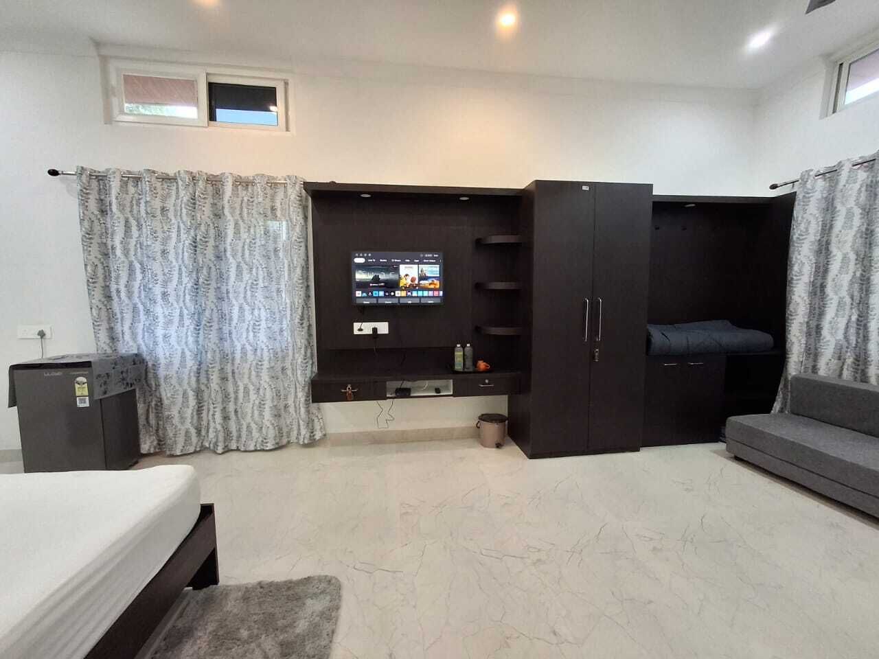 A modern living room with a flat-screen TV, built-in shelving, a sofa, and a bed.