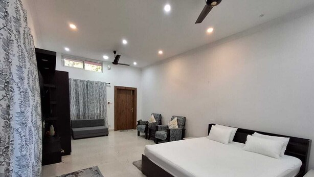 A bedroom with a large bed, a seating area with chairs, a wardrobe, and a staircase leading to another room.