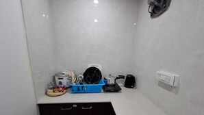 A small kitchenette with a stove, kettle, coffee maker, and a blue dish rack.