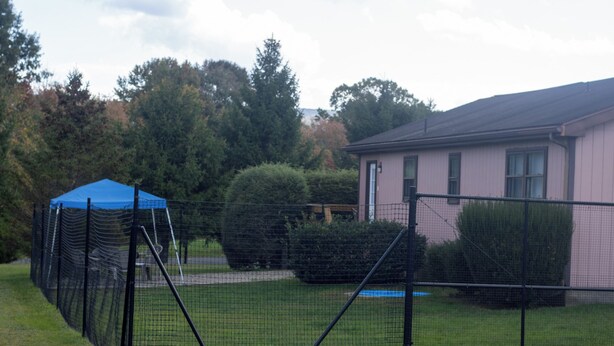 Een omheind buitengebied met een blauwe tent en een huis op de achtergrond.