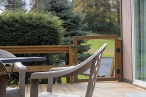 A wooden deck with a table and chairs, overlooking a garden with a wooden fence and trees.