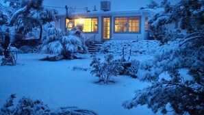 A modern house with a well-lit entrance and a snow-covered garden. - Cozy 2BR Home: Hot Tub, AC, Sauna, Fire, Near Park (Joshua Tree)