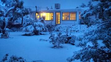 A modern house with a well-lit entrance and a snow-covered garden.