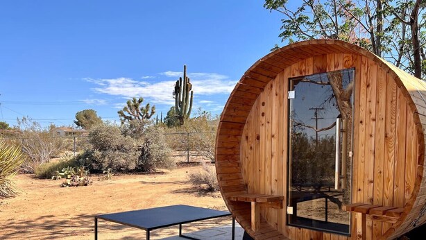 A wooden cylindrical structure with a glass door and a small table in front. - Cozy 2BR Home: Hot Tub, AC, Sauna, Fire, Near Park (Joshua Tree)