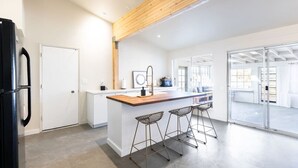 A modern kitchen with a wooden island, bar stools, and a large window. - Cozy 2BR Home: Hot Tub, AC, Sauna, Fire, Near Park (Joshua Tree)