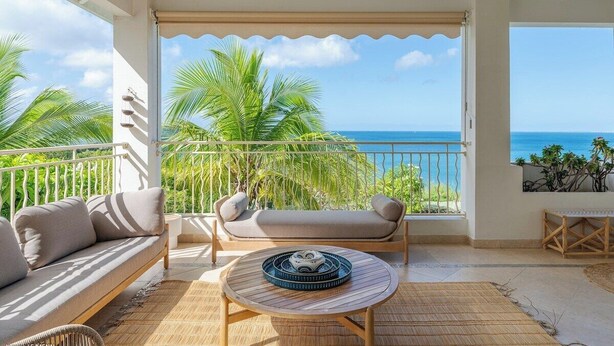 A balcony with a sofa and a round table, overlooking a clear blue sea and palm trees. - Sunset view, beach walk, heated pool (SAINT MARTIN)